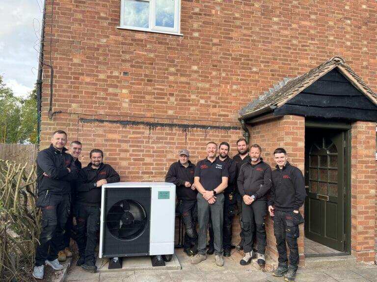 Group of Hereford Heating engineers standing outside a house next to a newly installed heat pump