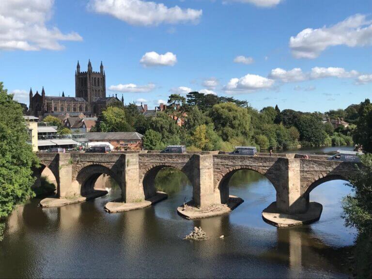 Two Hereford Heating vans driving across a bridge with Hereford Cathedral in the background