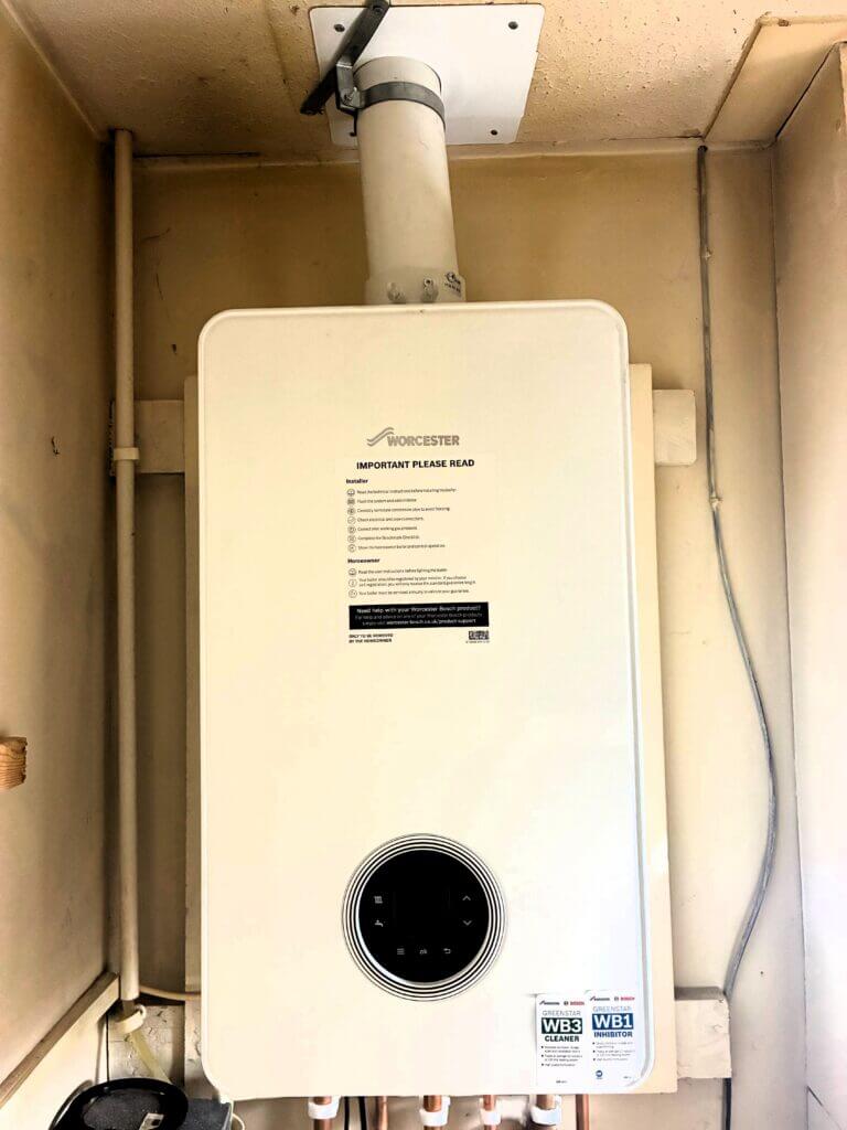 A Worcester Bosch boiler installed inside a utility cupboard with complex flue and ventilation piping